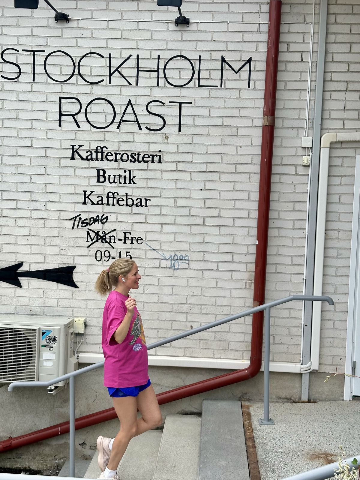 Amanda i rosa t-shirt springer uppför trappan förbi Stockholm Roasts vita tegelvägg
