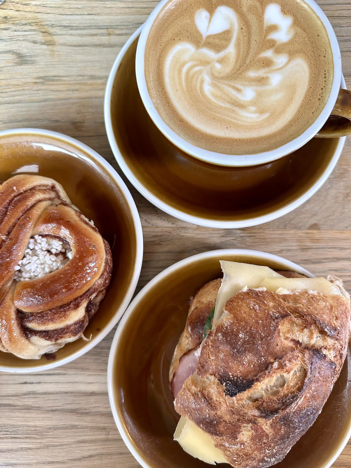 Kanelbullar, en macka och cappuccino på ett träbord hos Svedjan