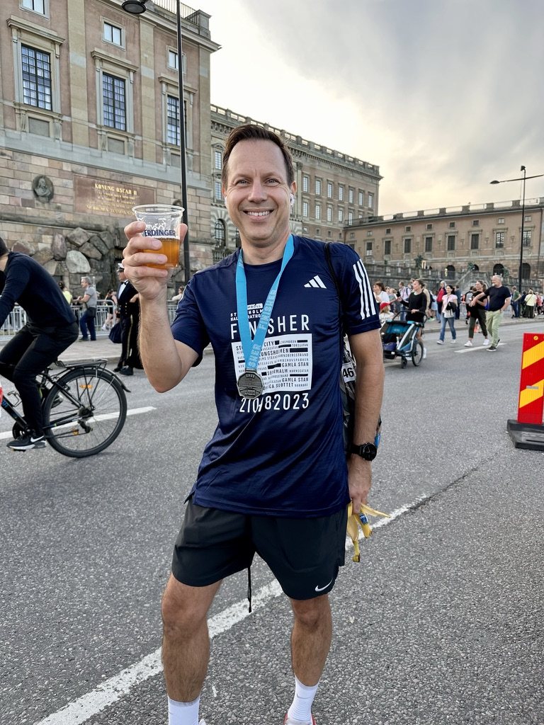 Löpare i finisher-tröja med medalj framför Kungliga Slottet efter Stockholm Halvmarathon