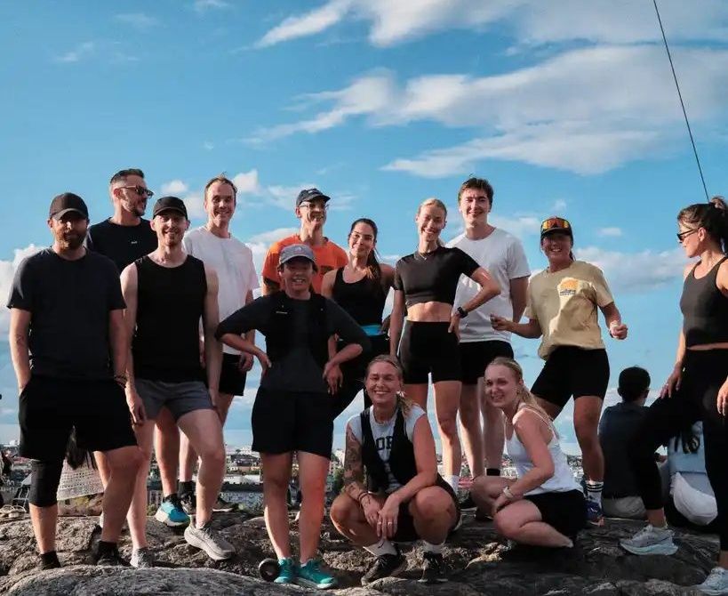 Ett tiotal löpare från Stockholm Summer Run Club samlade på en klippa i solsken med Stockholm i bakgrunden